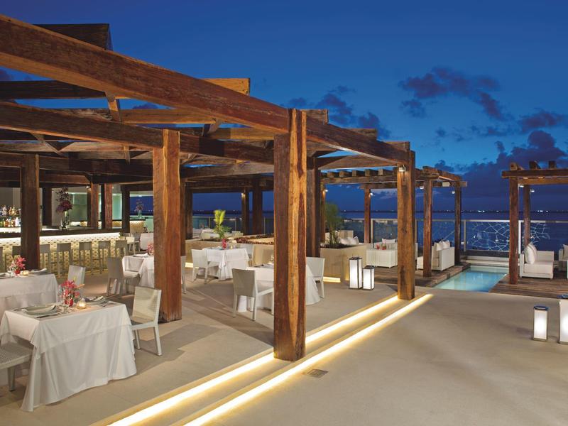 Open restaurant terrace with wooden beams and sea view at twilight.