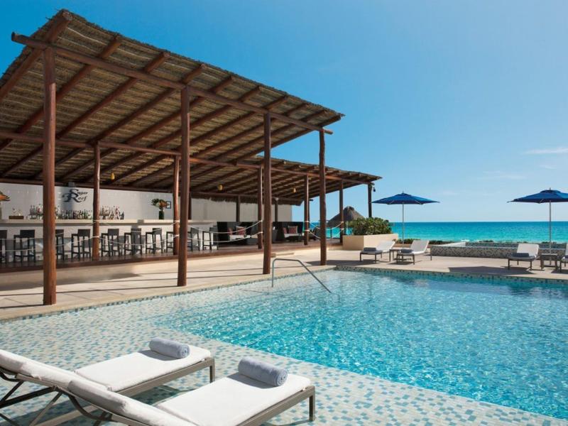 Modern outdoor pool area with sun loungers, umbrellas, and covered seating by the sea.