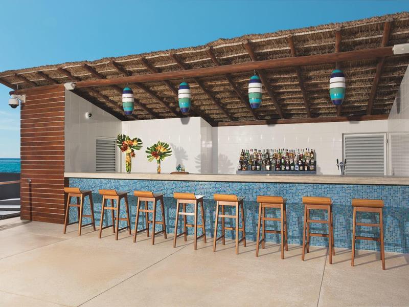 Outdoor bar with wooden stools under a pergola overlooking the sea.