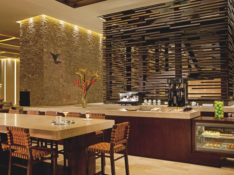 Modern hotel restaurant area with bar, wooden tables, and decorative lighting.