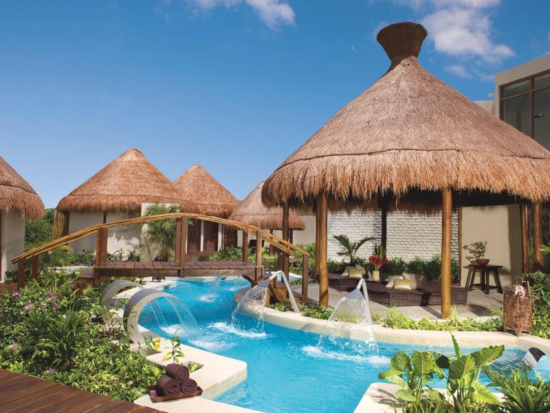 Bazén s vodopády a altány se doškovou střechou v tropickém hotelu.