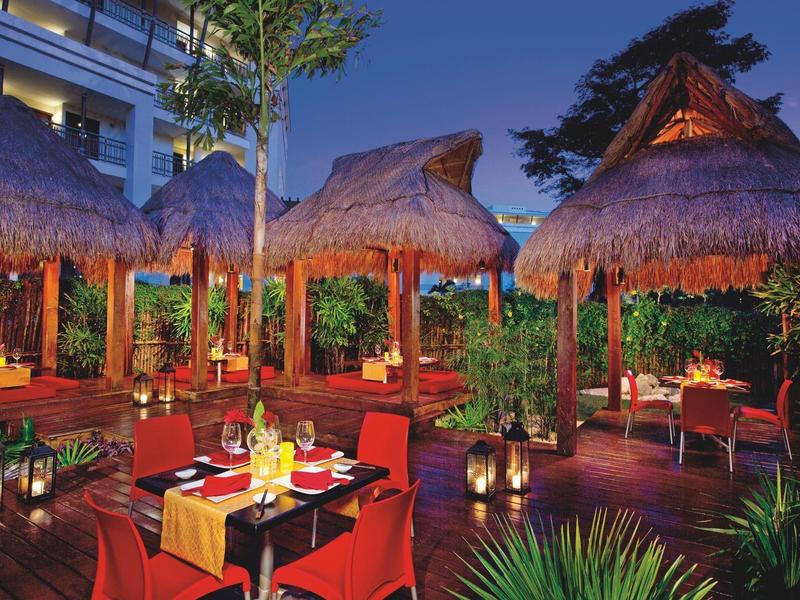 Večeře pod širým nebem pod doškovými střechami s atmosférickým osvětlením v tropickém prostředí.