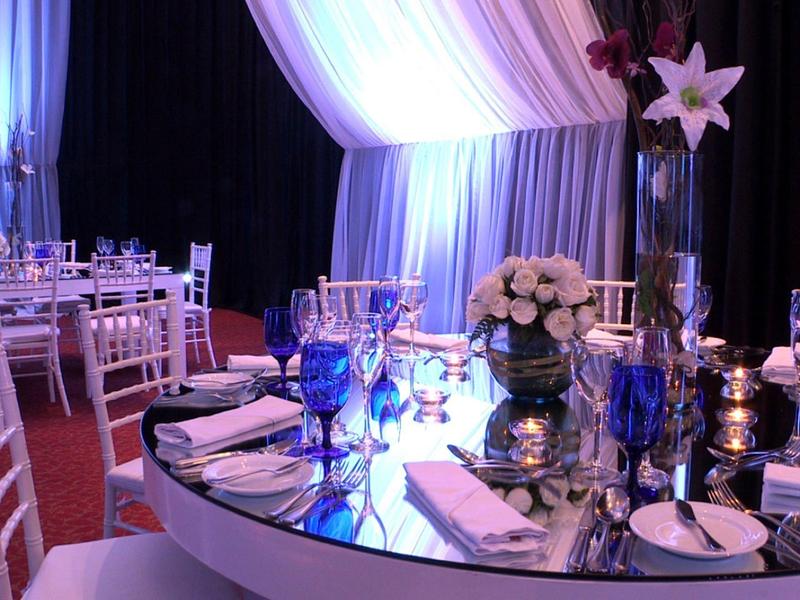 Elegantní kulatý stůl prostřený stříbrným příborem a květinovou výzdobou ve slavnostním prostředí.