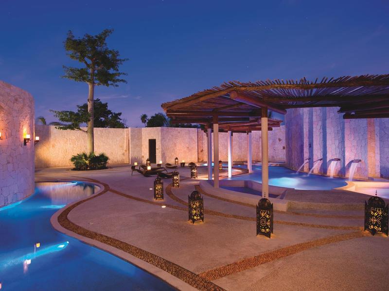 Terrazza serale con piscina, lanterne illuminate e aree salotto confortevoli in un hotel.