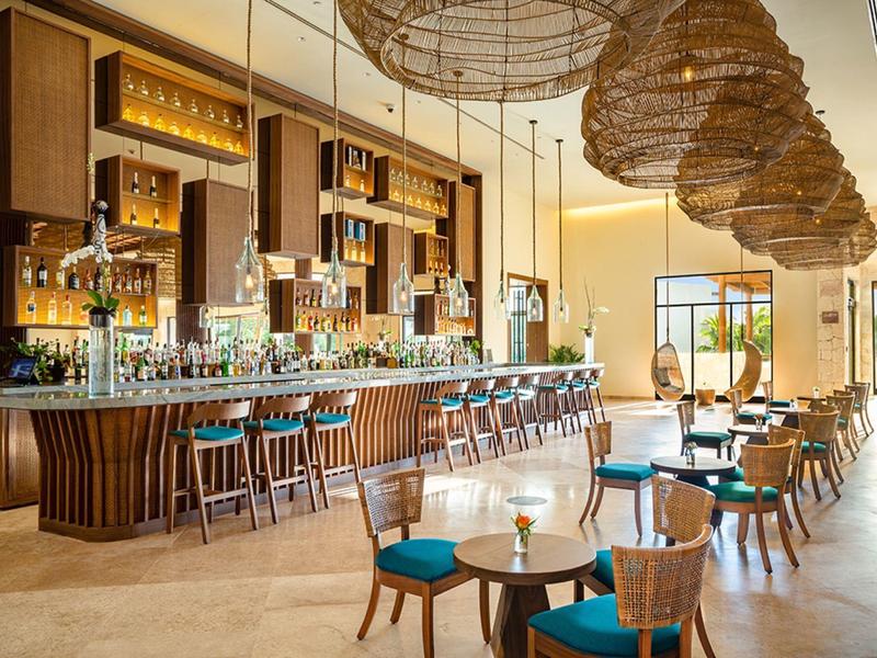 Bar dell’hotel luminosa con sedie in legno, sedili imbottiti blu e grandi lampade sospese.