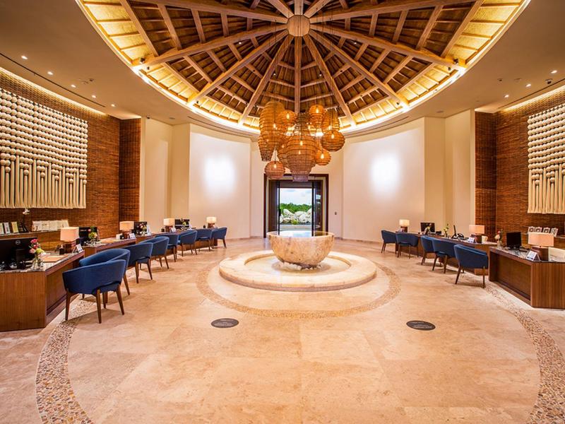 Lobby di hotel di lusso con camino rotondo, sedie blu e soffitto a cupola in legno.