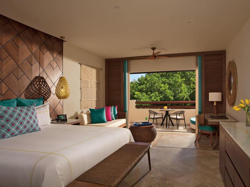 Camera d'hotel luminosa con letto matrimoniale, decorazioni colorate e balcone con vista sul verde.