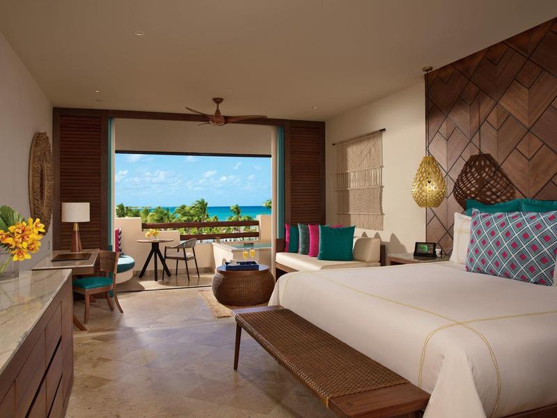 Camera d'hotel luminosa con letto grande, decorazioni in legno e vista su terrazza e mare.