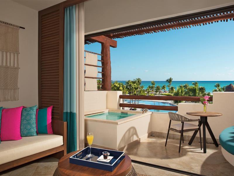 Balcone con vasca idromassaggio, area salotto e vista mare in una stanza d'hotel.