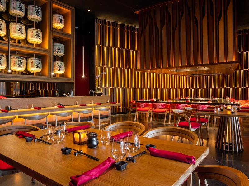 Bar d'hotel moderna con illuminazione calda, mobili in legno e aree salotto accoglienti.