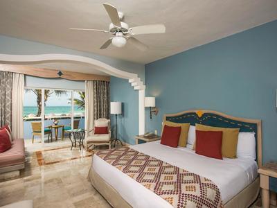 Habitación de hotel moderna con cama grande, ventilador de techo y balcón con vista al mar.