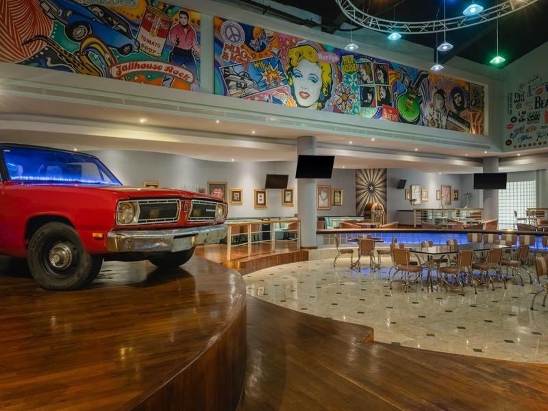 Ampia stanza con bar, posti a sedere e macchina rossa sul palco, murales colorati