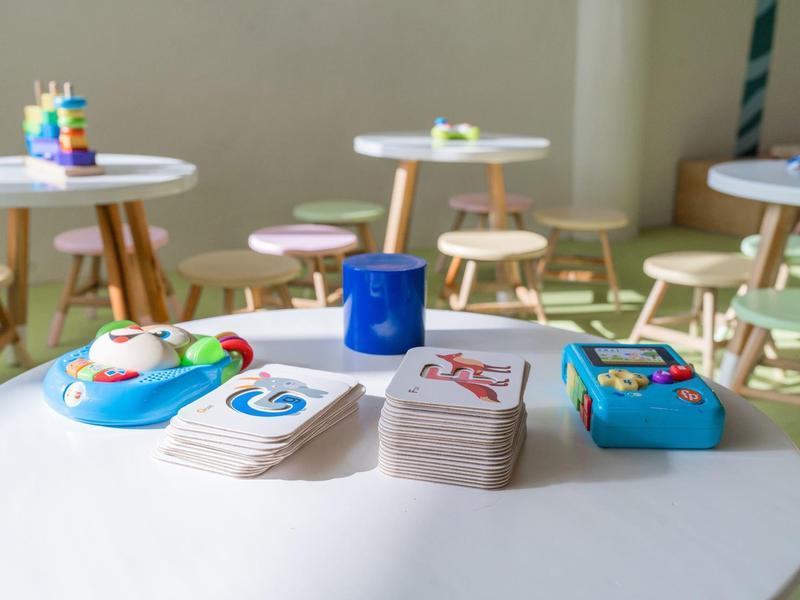 Giochi per bambini e carte da impilare su un tavolo rotondo bianco in una stanza di asilo con mobili in legno.