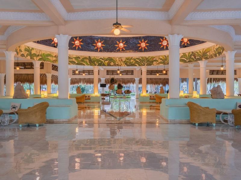 Ampia hall d'hotel con pavimento in marmo, colonne rotonde e aree salotto sotto un soffitto illuminato.