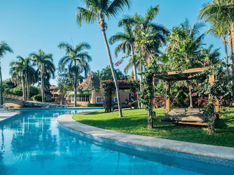 Piscina dell'hotel circondata da palme e paesaggio verde sotto un cielo limpido.