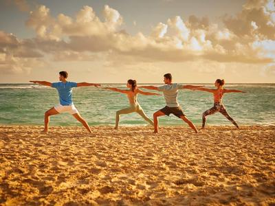 Vier Personen machen Yoga-Übungen am Strand bei Sonnenuntergang.