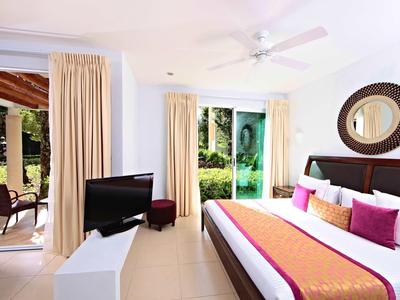 Camera d'hotel luminosa con letto grande, TV e accesso alla terrazza con vista sul giardino.