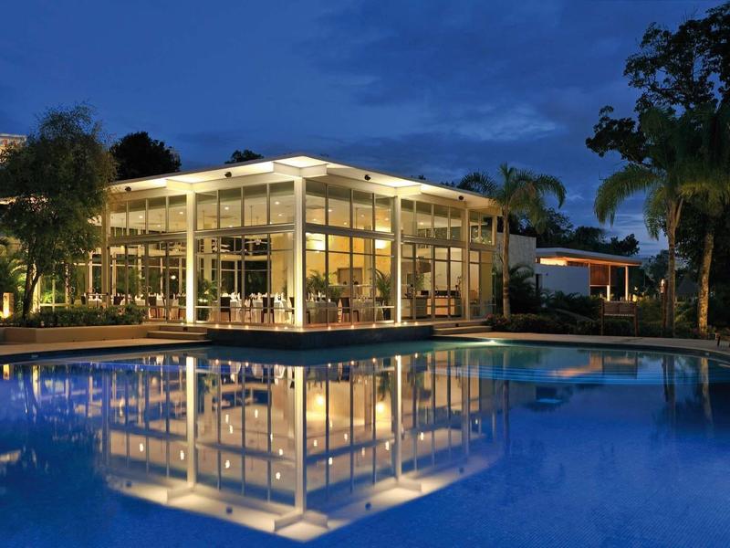 Edificio dell'hotel moderno con ampia facciata in vetro riflessa nella piscina illuminata.