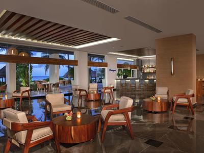 Ampio salone d'hotel con mobili in legno, illuminazione soffusa e grandi finestre con vista esterna.