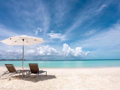 Zwei Strandliegen mit Sonnenschirm auf weißem Sand vor türkisblauem Meer und blauem Himmel.