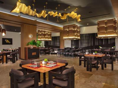 Ristorante moderno in hotel con tavoli di legno, sedie marroni e luci calde a sospensione.