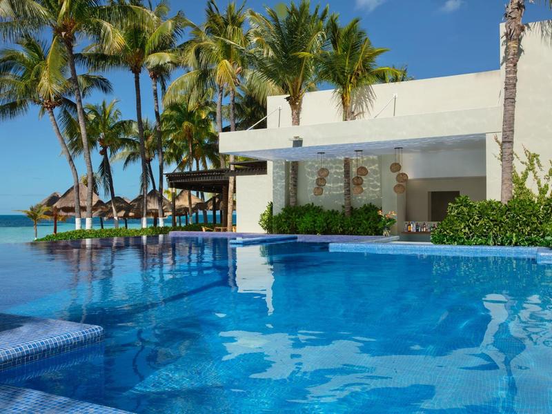 Resort con piscina blu, edificio bianco, palme e lettini sotto un cielo soleggiato