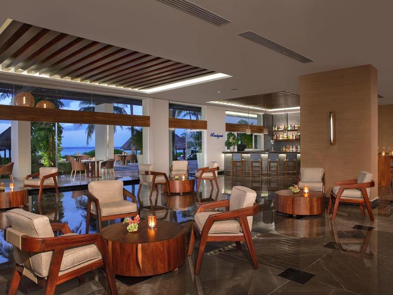 Ampio salone d'hotel con mobili in legno, illuminazione soffusa e grandi finestre con vista esterna.