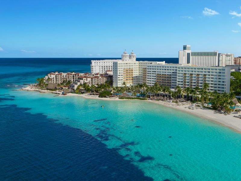 Resort alberghiero sulla costa con spiaggia di sabbia bianca e oceano turchese sotto un cielo azzurro.