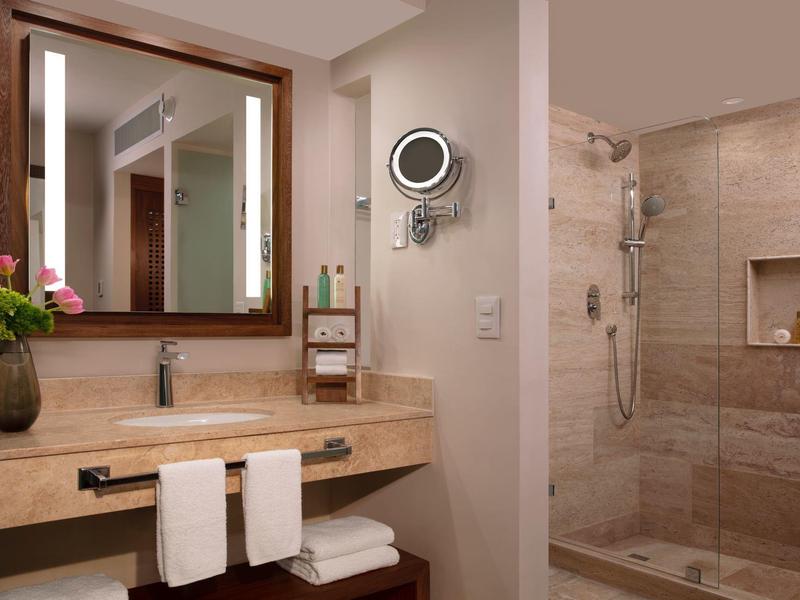 Bagno moderno in hotel con grande specchio, lavabo, asciugamani e doccia a filo pavimento.