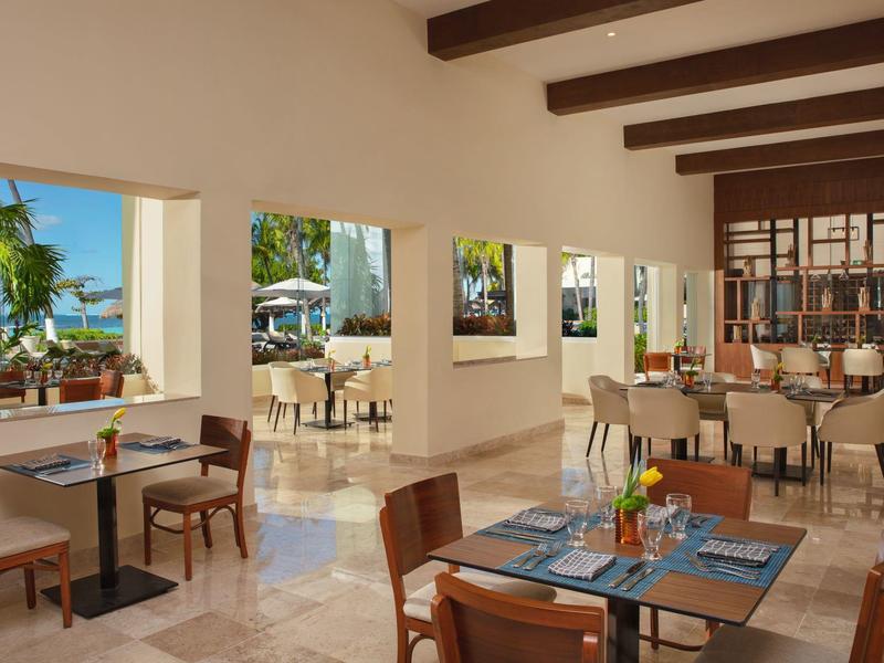 Zona pranzo luminosa dell'hotel con sedie in legno, tavoli e vista sul verde e piscina all'aperto.