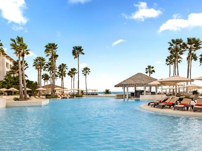 Grand piscine bleue avec parasols et palmiers dans un complexe hôtelier.
