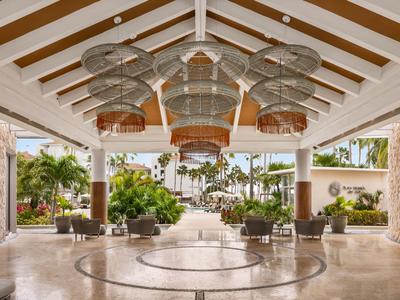 Lobby d'hôtel spacieuse et ouverte avec des lustres modernes et des plantes tropicales.
