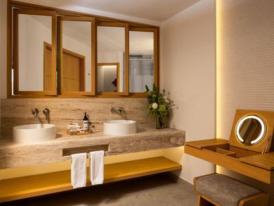 Salle de bain d'hôtel moderne avec doubles vasques, grand miroir et coiffeuse aux tons chauds.