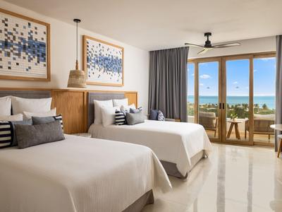 Chambre d'hôtel avec deux lits doubles, vue sur la mer et balcon avec chaises et table.