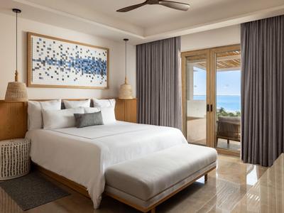 Chambre d'hôtel moderne avec grand lit, meubles en bois et vue sur la mer par des portes ouvertes.