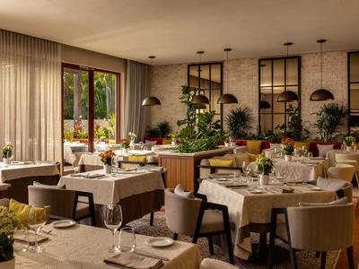 Restaurant lumineux avec tables dressées, décoration moderne et grandes fenêtres donnant sur un jardin.