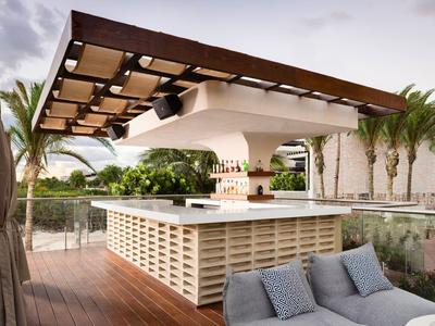 Bar extérieure moderne avec terrasse en bois, sièges lounge et palmiers en arrière-plan.