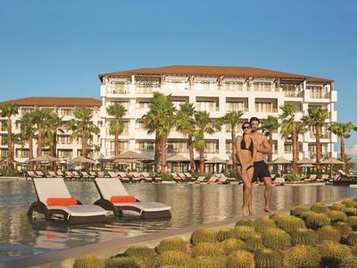 Hotel mit Pool, Sonnenliegen und Paar am Wasser bei sonnigem Himmel