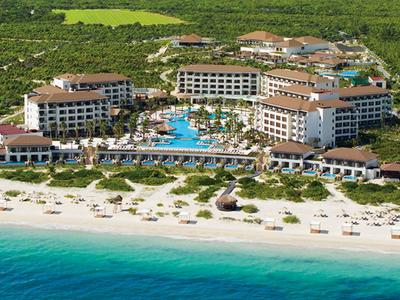 Großer Strandresort mit Pool, Sonnenliegen und tropischer Vegetation am Meer.