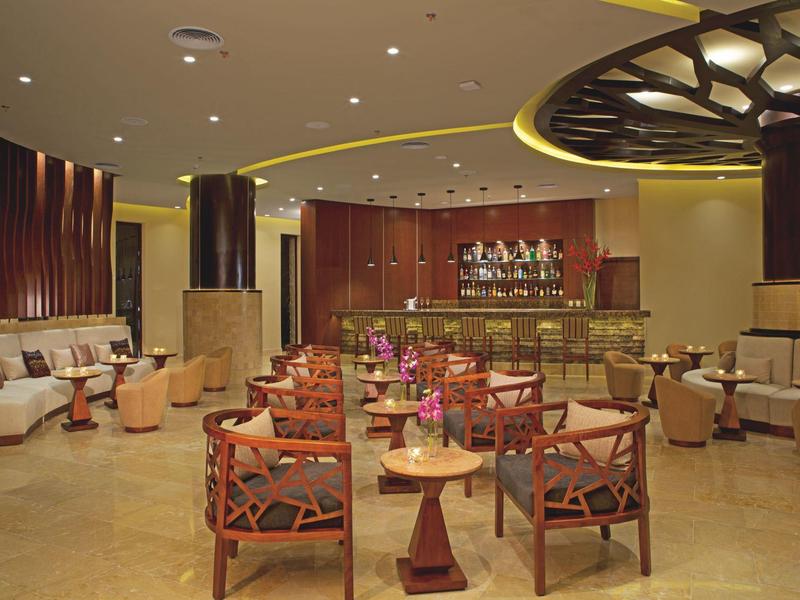 Lounge d'hotel elegante con sedie in legno, divani beige, tavoli rotondi e bancone bar chic.