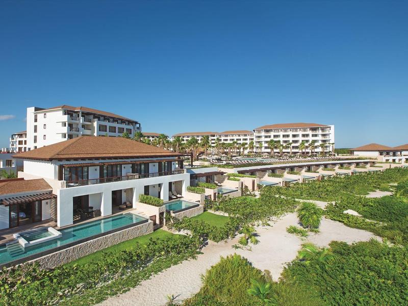 Grandi edifici bianchi del resort con piscine vicino al verde sotto un cielo azzurro limpido.