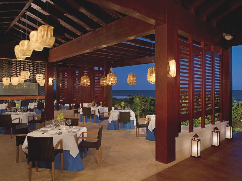 Ristorante elegante all'aperto con lanterne e vista sul mare al tramonto.