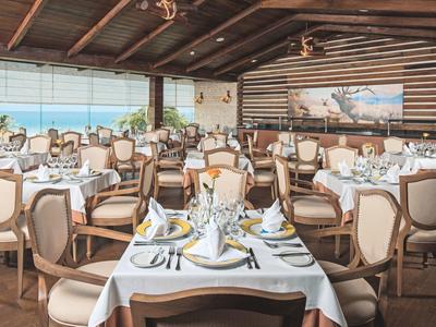 Elegancka restauracja z nakrytymi stolikami i widokiem na morze pod drewnianym stropem z belkami.