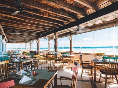 Zadaszony balkon z drewnianymi stołami i krzesłami, widok na morze pod jasnym niebem.