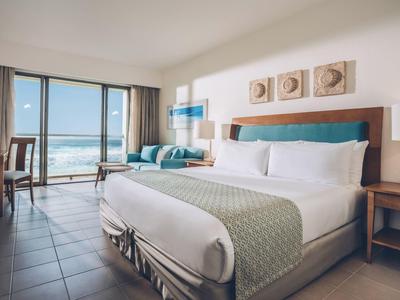 Nowoczesny pokój hotelowy z dużym łóżkiem, miejscem do siedzenia i widokiem na morze przez duże okna.