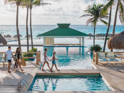 Vista di una piscina dell'hotel con palme e vista sull'oceano, persone che camminano lungo la piscina.