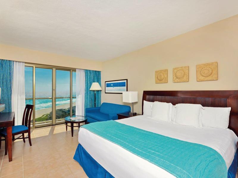 Jasny pokój hotelowy z widokiem na morze, łóżkiem king, biurkiem i balkonem.