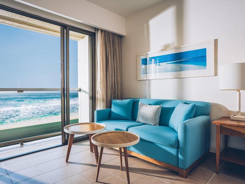 Nowoczesny salon z turkusową sofą, dwoma okrągłymi stolikami i widokiem na morze przez duże okna.