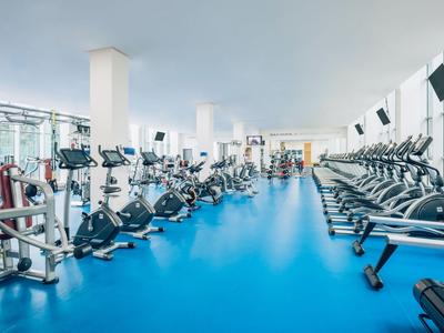 Duża siłownia z wieloma urządzeniami do ćwiczeń i niebieską podłogą