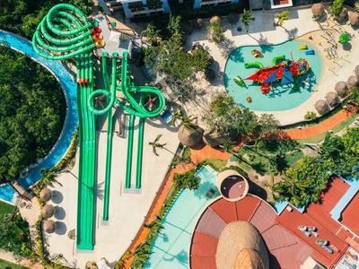Luftaufnahme eines Wasserparks mit grünen Wasserrutschen, Pool und buntem Spielfeld.